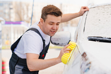 self-service car wash. a man in a work jumpsuit washes the car with a sponge 