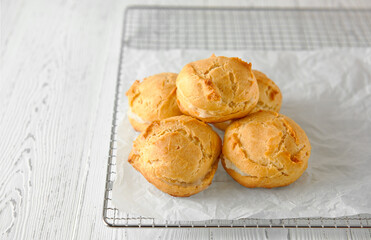 Homemade profiteroles or eclairs on a metal grid. Traditional French dessert. White wooden background. Close-up, copy space.