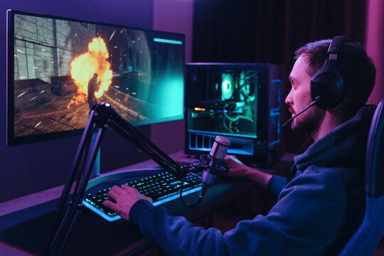 Concentrated young streamer man winning space shooter online competition talking at professional microphone in gaming room studio. Pro gamer playing online video games and streaming during tournament