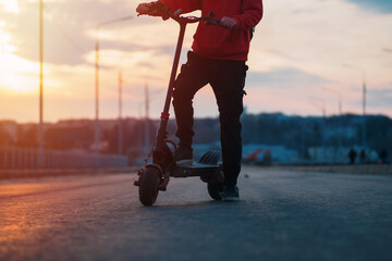 A man rides around the city on a powerful electric scooter. Road and sunset on the background