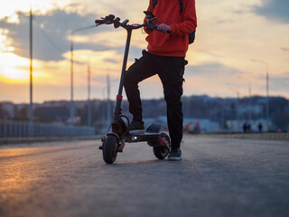 A man rides around the city on a powerful electric scooter. Road and sunset on the background