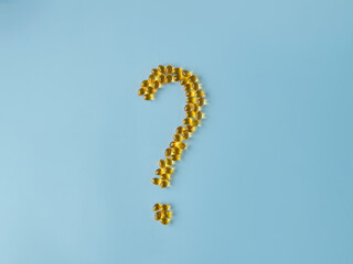 Vitamin capsules on a blue surface in the form of a question mark. Omega and vitamin D. Health care. Nutritional supplements. Opened bottle with yellow pills, tablets and capsules. Medicine questions.