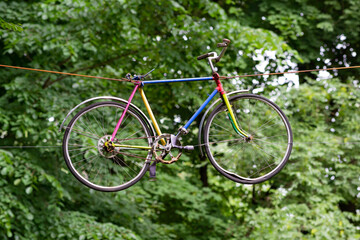 Fototapeta na wymiar A colorful bicycle hung on wires among the trees in the park.