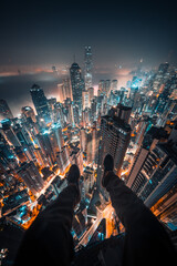 Futuristic cityscape at night with a daring man dangling his legs over the edge of a building