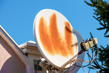 A rusty satellite dish on the wall of a red brick building. Wire connections are clearly visible...