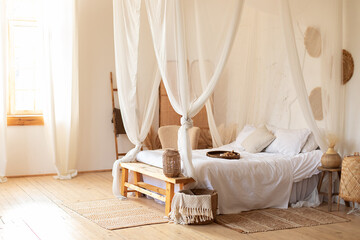 Fototapeta na wymiar Cozy scandinavian decoration room. hygge decor at home. interior white bedroom in boho style with coffe table,straw lamp and comfortable bed with pillows, copy space. bed with flowing white curtains 