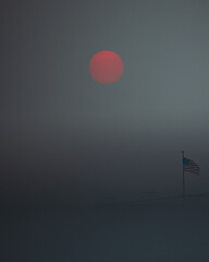 American flag waving outdoors on a foggy day with a blood moon in the background