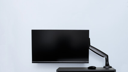 Modern thin computer monitor or TV set is mounted on a metal swivel desktop bracket with a gas lift function. Small black table. Off-center side holder. Copyspace