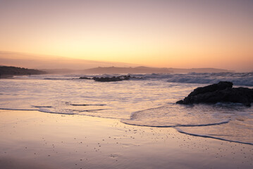 Beautiful dreamlike sunset on the beach with waves reaching the shore and rocks on the sand, Dunas de Liencres Natural Park and Costa Quebrada, Cantabria, Spain