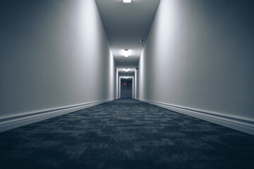 Long hallway with blue carpet and white walls with lighting lamps on the ceiling