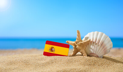 Fototapeta na wymiar Tropical beach with seashells and Spain flag. The concept of a paradise vacation on the beaches of Spain.