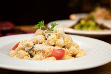 Closeup shot of gnocchi pasta with sauce, tomatoes and cheese in a white plate in a restaurant