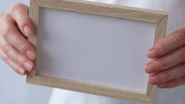 A woman is holding a frame with empty space in her hands. Then he points to the camera