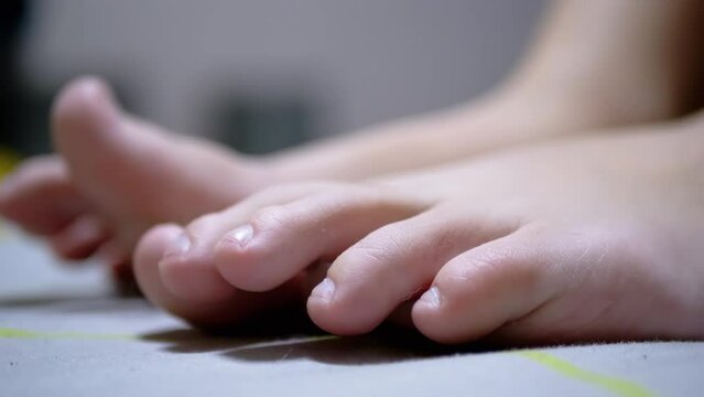 Close-up Tired Child Wiggles his Toes while Lying on the Bed in Room. Teen is moving fingers toes does gymnastics. Compression, unclenching of limbs, feet. Relief from cramps, stress, fatigue. Relax.