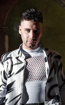 Studio portrait of a young man with direct light with shadows. Fashion trendy studio photo shoot with trendy clothes and isolated with black background