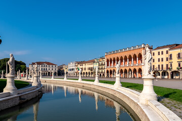 Fototapeta premium Scenic view on Prato della Valle, square in the city of Padua, Veneto, Italy, Europe. Green island at center, Isola Memmia surrounded by canal bordered by two rings of statues. Reflection in water