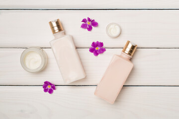 Cosmetic bottles and jars with flowers on wooden background, top view