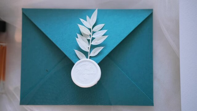 An exquisite envelope made of expensive textured paper is decorated with wax stamp and twig with leaves. Word wedding is written on seal. Stationery decor elements. Envelope for invitation and letter