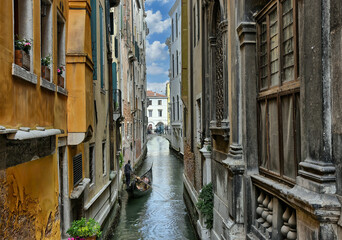  Vista de un angosto canal en Venecia con una góndola entre edificios. - obrazy, fototapety, plakaty