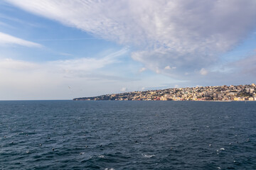Fototapeta na wymiar Panoramic view from Castel dell Ovo (Egg Castle) on the district of Posillipo in the city of Naples, Campania, Italy, Europe. Looking at the sea and the promenade. Clouds arriving, birds flying.