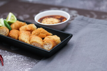 Fried spring rolls in a black plate served with tamarind dipping sauce on the table with black and gold placemats.