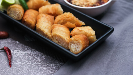 Fried spring rolls in a black plate served with tamarind dipping sauce on the table with black and gold placemats.