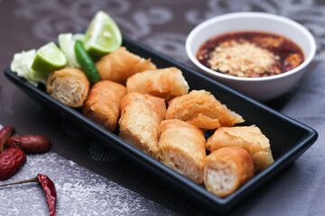 Fried spring rolls in a black plate served with tamarind dipping sauce on the table with black and gold placemats.
