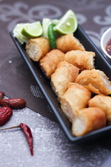 Fried spring rolls in a black plate served with tamarind dipping sauce on the table with black and gold placemats.
