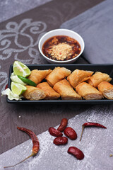 Fried spring rolls in a black plate served with tamarind dipping sauce on the table with black and gold placemats.