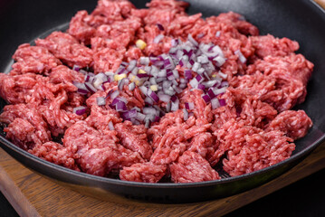 Fresh raw mince with spices and herbs on a dark concrete background