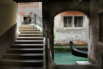 Fototapeta na wymiar Puente con escalera en Venecia sobre un canal y la punta de una góndola vista desde un pequeño embarcadero.