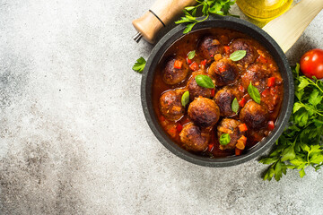 Meatballs in tomato sauce in a frying pan at light stone table. Top view copy space.