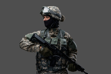 Shot of proud infantry dressed in protective costume holding rifle isolated on gray background.