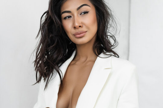 American Asian in a white cropped jacket over a naked body. Portrait of a stylish sexy brunette with curls and makeup