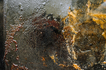 Texture, background, top view of a black tray smeared in fat, oil, pieces of meat, after cooking the dish. Photography, abstraction.