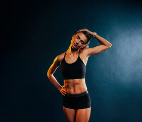Fototapeta na wymiar Young muscular woman warming up her neck before training against black background