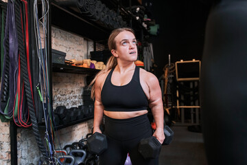 Woman with achondroplasia disorder holding two dumbbells and looking away