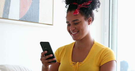 Happy black girl celebrates success with fist reading content on smartphone from home