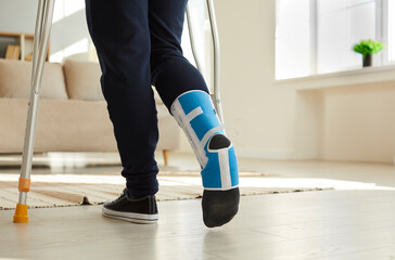 Person with broken foot walking on crutches. Young man wearing ankle support brace or fracture...
