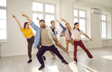 Group of energetic hip hop dancers have fun rehearsing dance moves while learning new dance. Talented young people in casual clothes dance together in bright and spacious dance studio.