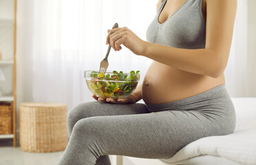 Crop shot of healthy sporty pregnant woman eat tasty vegetable salad. Future mother enjoy delicious vegetarian lunch or dinner take care of health during pregnancy. Motherhood and healthcare.