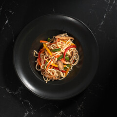 Japanese udon noodles fried in a wok. Udon noodles with vegetables on a dark background.