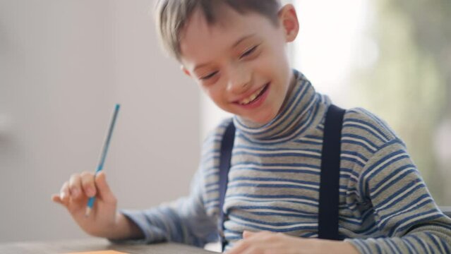 Smiling excited autistic child drawing as woman pointing talking. Portrait of happy confident Caucasian boy with mental illness studying at home with mother. Autism and family concept