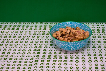 Tasty organic pistachios in a flowery bowl on top of a white table with green circles