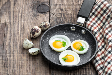 Fried quail eggs in onion ring in frying pan on wooden table