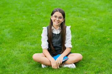 smiling child in glasses sitting on green grass with book