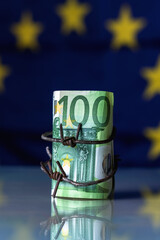 European Union currency wrapped in barbed wire against flag of EU as symbol of Economic warfare, sanctions and embargo busting. Vertical image. - obrazy, fototapety, plakaty