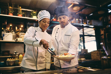 Two chefs serving dish while working at restaurant kitchen.