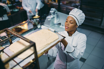 Above view of African American professional cook taking tray with food from cooling rack.