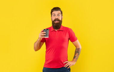Surprised bearded man in casual red tshirt holding coffee cup with arm akimbo, takeaway